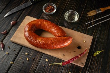 Chorizo sosisi ahşap bir kesme tahtasına oturur. Yakınlarda baharatlar ve bir bıçak var. Sahne bir mutfak ortamında, bazı aletlerle düzenleniyor..