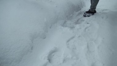 Gri pantolonlu ve siyah ayakkabılı bir birey geçitten kar küreyerek derin karda görünür bir yol açar. Bölgeyi çevreleyen kış manzarası ve karla kaplı bir zemin oluşturur.