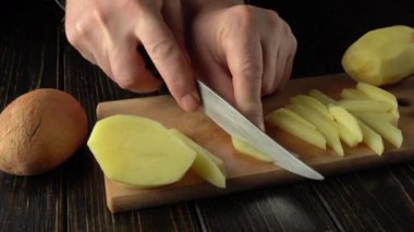 Eller patatesleri ustalıkla ince şeritler halinde dilimliyor. Kesme işleminin net bir şekilde ilerlemesini sağlayan tam bir patates ve ek dilimler var.