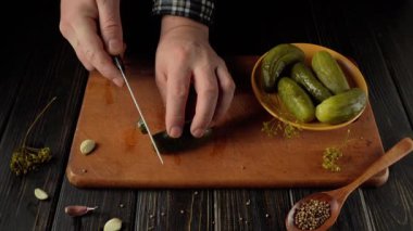 Elleri ustalıkla bir ahşap kesim tahtasının üzerinde turşuları dilimliyor. Yanında bir kase turşu ve etrafa saçılmış baharatlar var. Mutfak aktiviteleriyle dolu sıcak bir mutfak atmosferi yaratıyor.