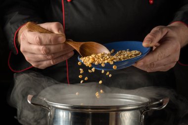 Bir şef, bir tencereye mavi kaseden sarı bezelye ekliyor. Şef mutfakta bir tabak hazırlarken tencereden buhar yükselir. Akşam oldu ve şef işine odaklandı..