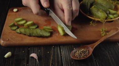 Tahta kesme tahtasında turşu dilimlemek, ellerinde bıçak, etrafa saçılmış sarımsak karanfilleri ve baharatlarla mutfak ortamındaki yemek hazırlama sürecini vurgulamak.