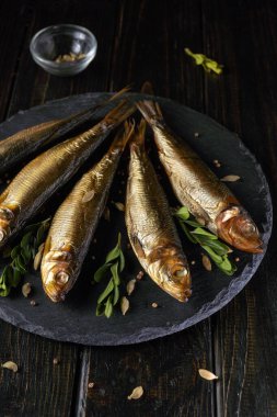 Dört parça taze füme balık siyah bir tabağa konur. Yeşil otlar ve küçük baharatlar balığı çevreleyip lezzet katıyor. Bu yemek günün herhangi bir saatinde yemek için hazır görünüyor..