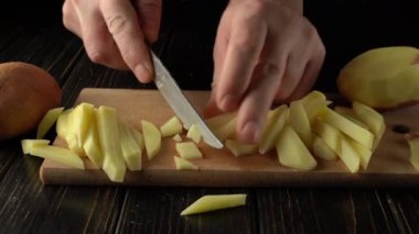 Elleri patatesleri ustalıkla ahşap bir kesim tahtasının üzerinde çeşitli şekillerde dilimliyor, kırsal mutfak ayarları görülebilir, sürekli yemek hazırlama ve kesme tekniklerini vurguluyor.