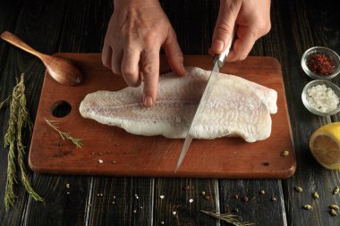 Bir insan mutfaktaki tahta bir tahtada balık kesiyor. Yakınlarda baharat ve limon var. Ellerinde bir bıçak var, balığı pişirmeye odaklanmış..