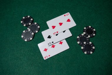 Siyah poker çiplerinin yanında yeşil bir keçeli masa üzerinde üç iskambil kartı var. Akşam arkadaşlarla ya da ailelerle poker oynanıyor.