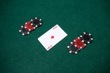 İki tarafında poker fişleri olan yeşil bir masada bir karo ası yatıyor. Sahne bir kart oyunu için ayarlandı.