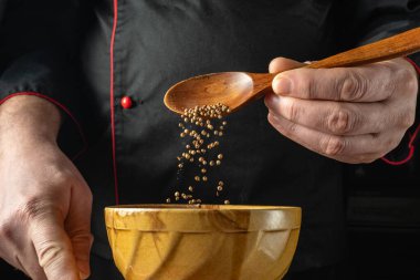 Bir şef ahşap bir kaşıktan küçük tohumları ahşap bir kaseye döküyor. Mutfak aletler ve malzemelerle aydınlık. Bu gün içinde gerçekleşir..