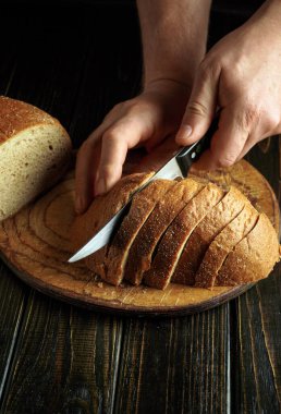Eller bir somun taze ekmeği ahşap kesme tahtasıyla dikkatlice dilimliyor. Samimi mutfak atmosferi sahnenin kırsal çekiciliğini vurguluyor..