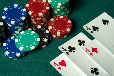 Yeşil bir masada üst üste yığılmış poker fişleri olan bir kart oyunu, kartlarınızı dört çeşit ya da dörtlü olarak gösteriyorsunuz. Sahne canlı, odaklanmış ve kumar oynuyor..