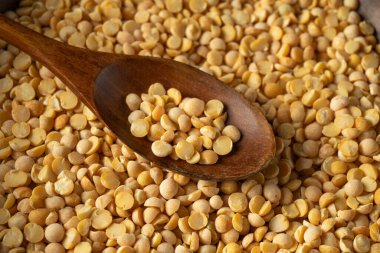 Ahşap bir kaşık sarı bezelye yığının üzerinde duruyor. Kaşık bezelye içerirken diğerleri yüzeyi kaplıyor. Sahne çiğ yemek hazırlıyor..