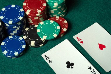 Renkli poker fişleri yakınlarda istiflenirken iki iskambil kartı as gösteriyor. Arkadaşlar oyun gecesinin tadını çıkarmak için yeşil bir masanın etrafında toplanırlar. Atmosfer canlı ve eğlenceli..