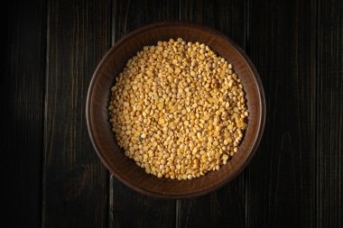 Yuvarlak bir ahşap kase koyu bir ahşap masaya yerleştirilmiş büyük miktarda bölünmüş sarı bezelye içerir. Bezelyeler kurudu ve kâsede eşit şekilde oturuyorlar. Işık kâseyi aydınlatır..