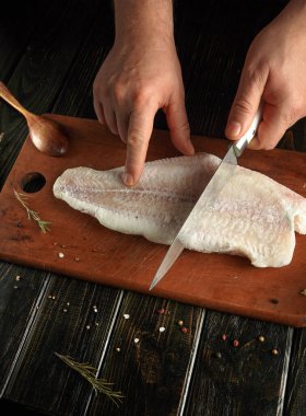 Tahta kesme tahtasından taze balık kesiyor. Mutfak iyi aydınlatılmış ve çeşitli otlar ve baharatlar etrafa saçılmış..