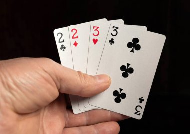 Bir adam elinde dört tane iskambil kağıdı tutuyor, iki tane üçlü ve iki tane ikili gösteriyor. Bu bir poker oyunundan bir an, muhtemelen bir kumarhanede..