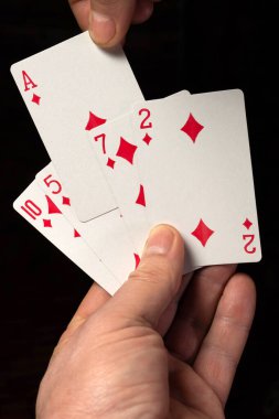 Bir elinde elmas takım elbisenin bir kaç iskambil kağıdını tutarken diğer elinde desteden bir as çekiyor. Karanlık ortam bir gece kumarhanesi oyunu olduğunu gösteriyor..