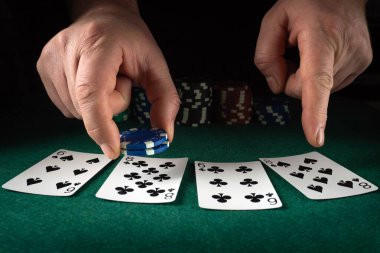 Bir insan masaya çip koyarken kartlara odaklanır. Sahne, arka planda çipler olan bir poker oyununun el pozisyonunu gösteriyor..