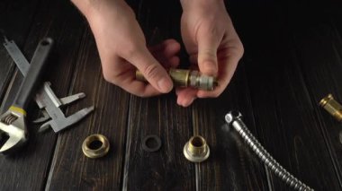 Elleri pirinç tesisat tesisatı montajı, konnektörler ve T-joint, ahşap bir çalışma yüzeyinde çeşitli araçlar ve parçalarla düzenlenmiş, karmaşık montaj işlemini vurgulayan