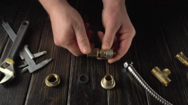 Tahta tezgah üzerindeki tesisat tesisatlarını bağlayan usta elleri, çeşitli araç gereçler ve bileşenler sıralanmış, bir atölye ortamında montaj sürecini gösteren.