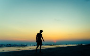 Sahilde günbatımı zamanında yürüyen siluet adam
