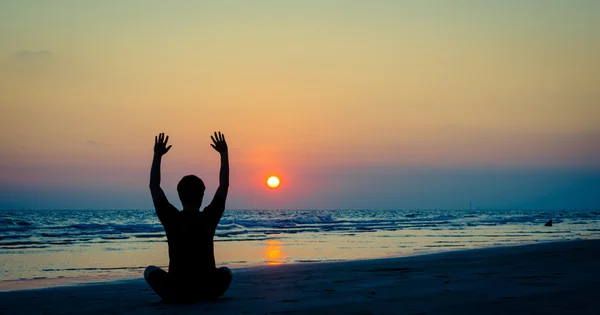 Man silhouet doen yoga oefening in sunset beach Rechtenvrije Stockfoto's