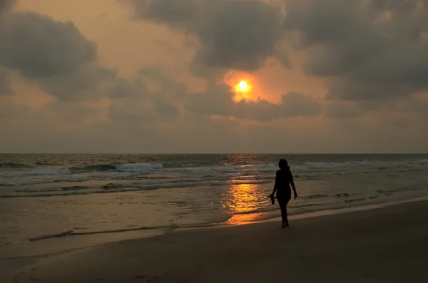 Silueta mujer caminando en la playa en la hora de la puesta del sol Imagen de archivo