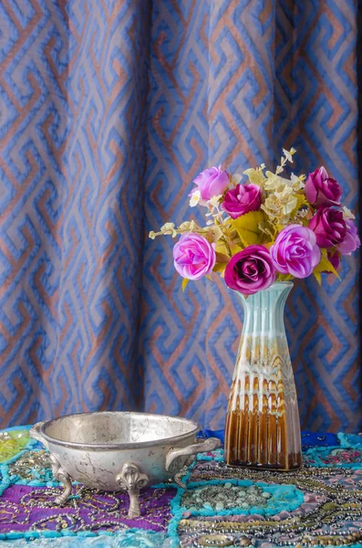 Cuenco de metal marroquí colocado sobre una mesa con un jarrón de flores . Imágenes De Stock Sin Royalties Gratis