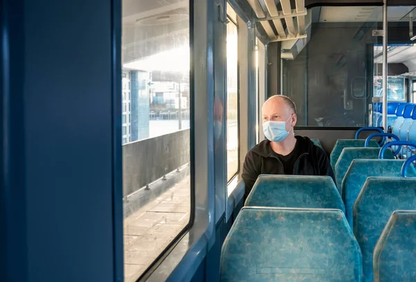 Serious man wearing surgical mask looking through the window in a train