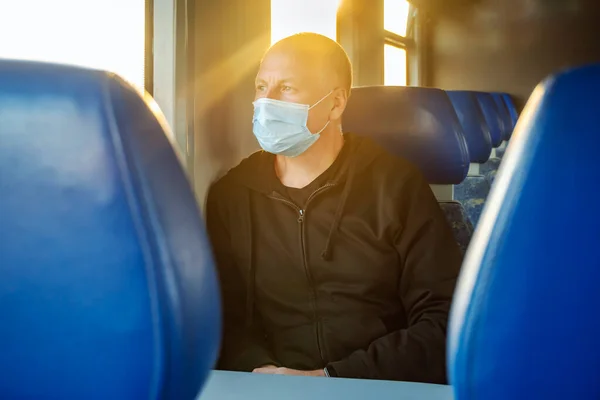 Serious man wearing surgical mask looking through the window in a train