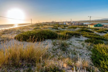Günbatımında kum tepeleri ve yürüyüş yolları olan geniş kumlu Faro plajı, Faro, Algarve, Portekiz