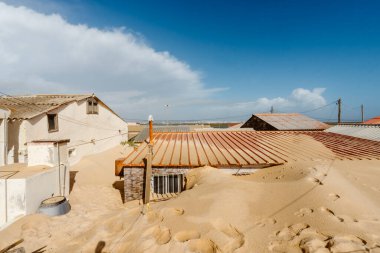 Portekiz 'in Faro Sahili' ndeki küçük geleneksel balıkçıların evleri, şiddetli kış fırtınaları sonrasında neredeyse tamamen kuma gömüldü. Kapılar, pencereler ve girişler, kıyı aşınmasının ve güçlü rüzgarların çarpıcı etkisini vurgulayarak kapatıldı. Bu sce