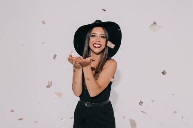 Moda kızı, kapalı mekanda fotoğraf çekerken komik suratlar yapıyor. Konfetilerle poz veren ve kameraya gülen mutlu bir kadın. Tatil, doğum günü, yeni yıl. Yüksek kalite fotoğraf