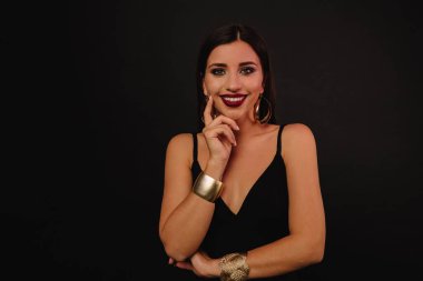 Güzel küpeli gülümseyen bayan siyah arka planda poz veriyor. Güzel makyajlı esmer kadın izole arkaplanda kameraya bakıyor. Yüksek kalite fotoğraf