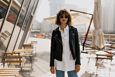 Açık terasta poz veren gülümseyen siyah saçlı kadın. Güzel genç bayan şehirde kendini mutlu hissediyor. Yüksek kalite fotoğraf