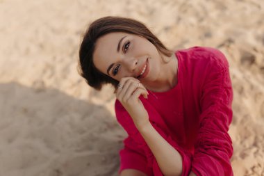 Sahilde dinlenen ve kameraya gülümseyen koyu renk saçlı hoş bir kadın. Yüksek kalite fotoğraf