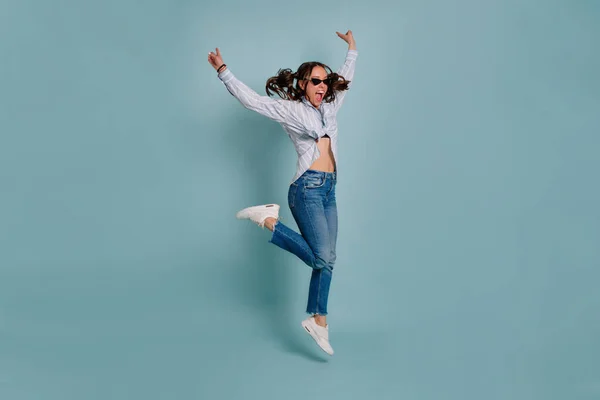 Full-lenght portrait of funny lovely female model jumping and having fun over isolated background. Happy girl dances and smiles on blue isolated background.