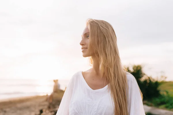 Porträt einer hinreißenden Europäerin mit langen Haaren und weißem T-Shirt, die im Sommerresort über der Küste steht — Stockfoto