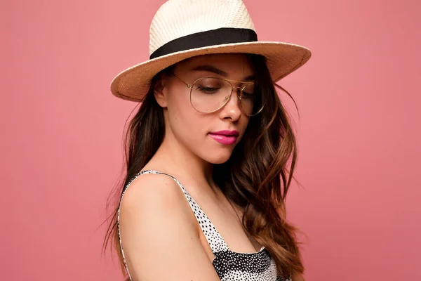 Wanita cantik yang menarik dengan rambut bergelombang di topi dan kacamata dengan bibir merah muda berpose di atas latar belakang merah muda — Stok Foto