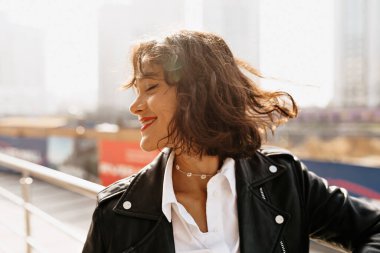 Kısa saçlı, neşeli bir bayan. Güneş ışığının tadını çıkarıyor ve şehirde eğleniyor.