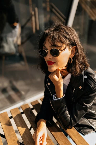 Wanita bergaya berkacamata dengan lipstik merah duduk di teras yang cerah dan menunggu teman-teman — Stok Foto