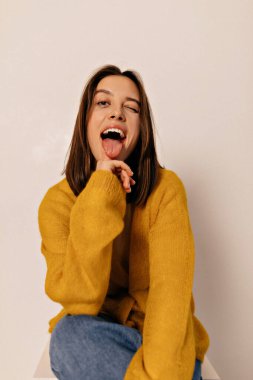 Dar kısa saçlı, sarı ceketli güzel bir bayanın portresi izole edilmiş arka planda dilini gösteriyor. Yüksek kalite fotoğraf