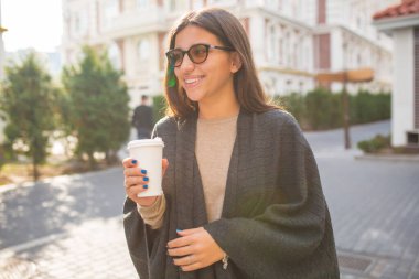 Harika bir stil sahibi kadın. Koyu uzun saçlı. Güneşli bir sokakta sabah kahvesiyle yürüyor. Yüksek kalite fotoğraf