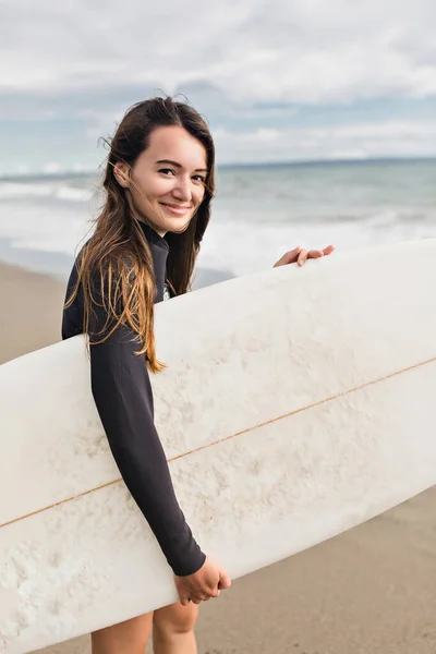 Portrait of charming stylish woman with surfboard posing at camera with smile on the beach. High quality photo