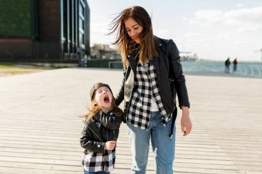 Çekici küçük kız dışarı çıktı, eğleniyor ve annesiyle birlikte deniz kenarında yürüyordu. Siyah pantolonlu ve spor ayakkabılı bir kadın kızıyla vakit geçiriyor. Yüksek kalite fotoğraf