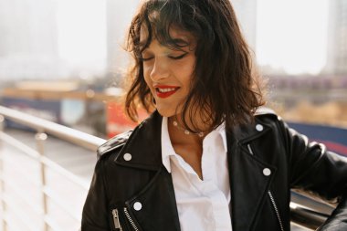 Kırmızı dudaklı, beyaz bluzlu, siyah ceketli, güneş bağıyla gülümseyen romantik bir kız. Yüksek kalite fotoğraf