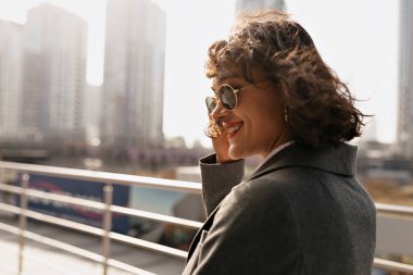 Güneş gözlüğü takan, gülümseyen ve yazın tadını çıkaran sevimli, uçan saçı olan bir kızın dış portresini yakından çek. Yüksek kalite fotoğraf
