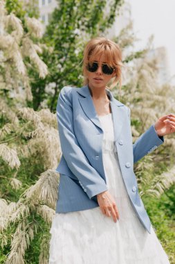 Açık havada poz veren zarif genç bir kadının güzel portresi. Saf yüzlü, açık renk elbiseli, yeşil bitkilere karşı poz veren çekici bir bayan. Yüksek kalite fotoğraf