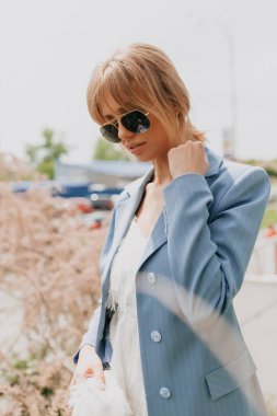 Tasma tutan ve güneşli şehirde poz veren bir kızın sokak portresi. Çekici sarışın kadın, gülümsüyor ve aşağıya bakıyor. Yüksek kalite fotoğraf