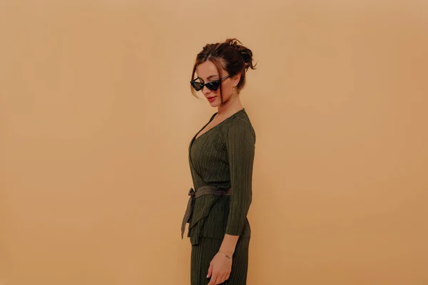 Elegante chica moderna en traje y gafas mirando hacia abajo y sonriendo sobre fondo beige. Retrato interior de una joven empresaria —  Fotos de Stock