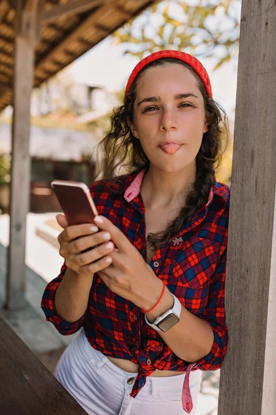 Wanita lucu menawan di cap scrolling smartphone dan membuat wajah-wajah di luar pada hari musim panas Stok Foto Bebas Royalti